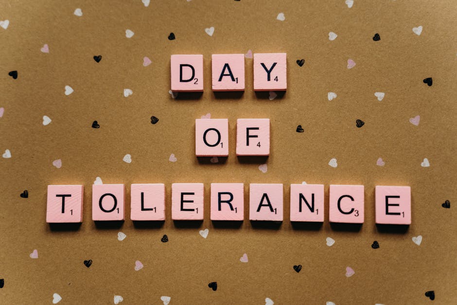 Napisy "Dzień Tolerancji" wykonane z różowych liter na tle brązowego papieru z serduszkami. Idealne do podkreślenia wartości tolerancji i akceptacji.